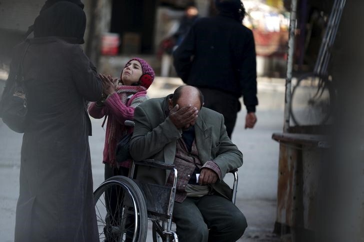 © Reuters. A girl with her father on a wheel chair, ask for help to pay a medical bill from passers by, in Douma, Syria