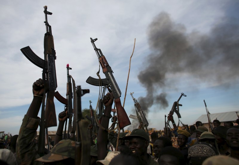 © Reuters. Rebel fighters hold up their rifles as they walk in front of a bushfire in a rebel-controlled territory in Upper Nile State 