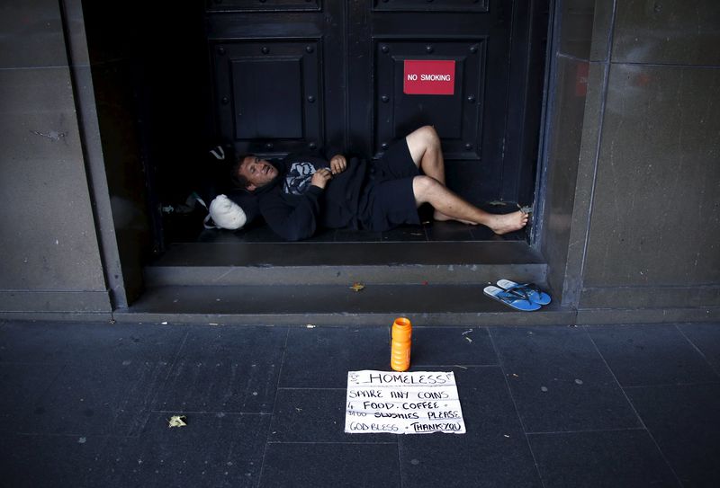 © Reuters. A man begs for money as he lies in the emergency exit doorway of a building in central Sydney