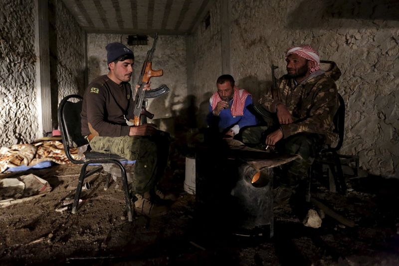 © Reuters. Rebel fighters of the Al-Furqan brigade keep warm by a fire with their weapons in Aziziyah village, southern Aleppo countryside