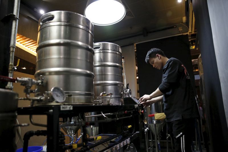 © Reuters. Craft beer brewer Huang Yijun checks a brewing machine at microbrewery NBeer Pub in Beijing