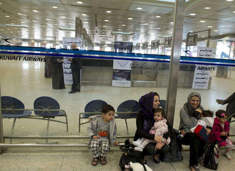 © Reuters. File picture of passengers sitting outside the Kuwait Airways terminal area at the Kuwait International Airport