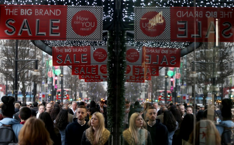 © Reuters. Shoppers are reflected in a store window as they pass sales advertisements on Oxford Street in London, Britain