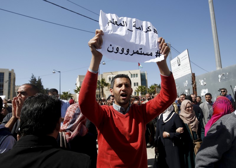 © Reuters. Palestinian teacher holds a sign that reads "Teacher's dignity, we will continue" during a protest demanding better pay and conditions, in the West Bank city of Ramallah