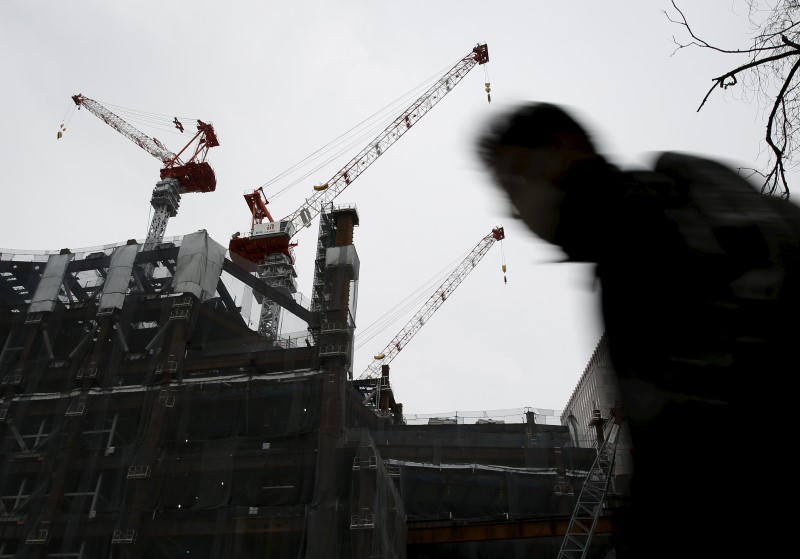 © Reuters. A man walks under cranes on a building under construction at a central business district in Tokyo