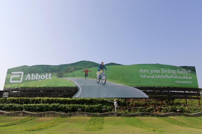 © Reuters. File picture shows a worker watering plants next to an advertisement billboard of Abbott in Mumbai, India