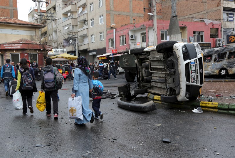 © Reuters. Residents walk by a vehicle, which was damaged during the clashes between security forces and Kurdish militants, as they flee after clashes between security forces and Kurdish militants from Baglar district, which is partially under curfew, in Diyarbakir