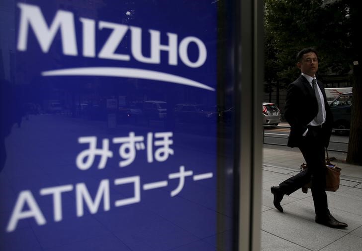 © Reuters. A man walks past a signboard of Mizuho Bank ATM outside its headquarters in Tokyo