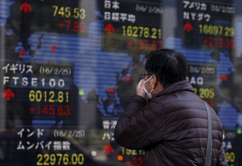 © Reuters. A pedestrian looks at an electronic board showing the stock market indices of various countries outside a brokerage in Tokyo