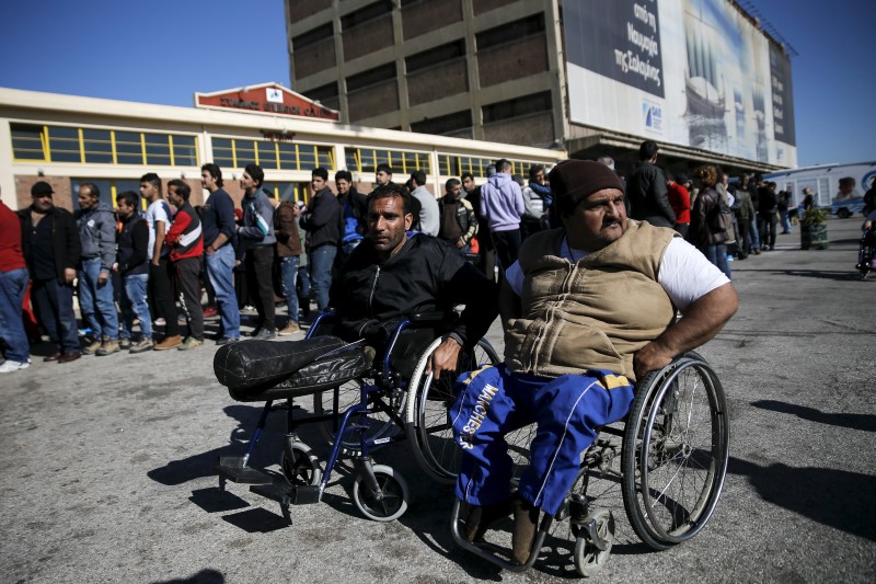 © Reuters. Syrian refugee Sheikho, and Iraqi refugee Omar, both on wheelchairs, wait for a food distribution as refugees and migrants line up outside a passenger terminal used as shelter at the port of Piraeus, near Athens