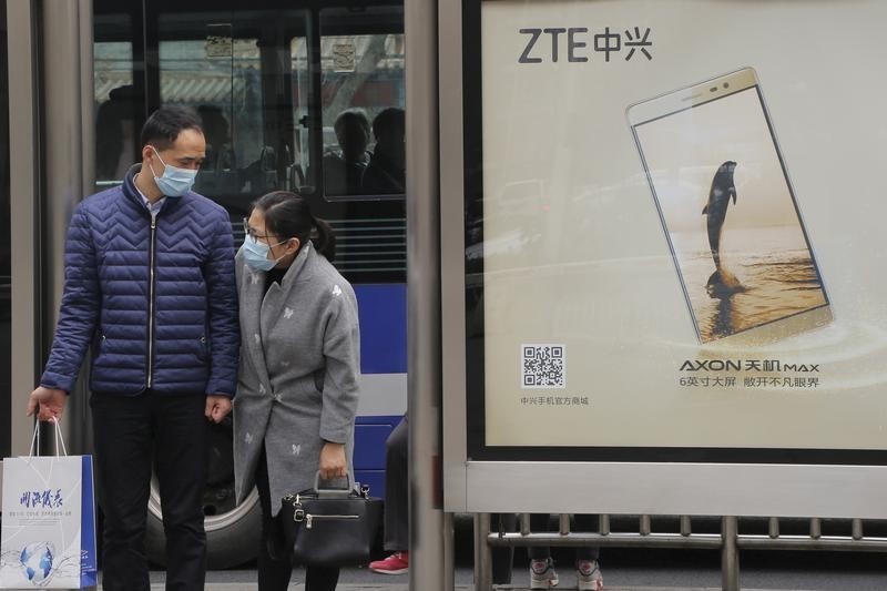 © Reuters. People wearing facial masks stand next to an advertisement board of ZTE's mobile phone at a bus stop in Beijing