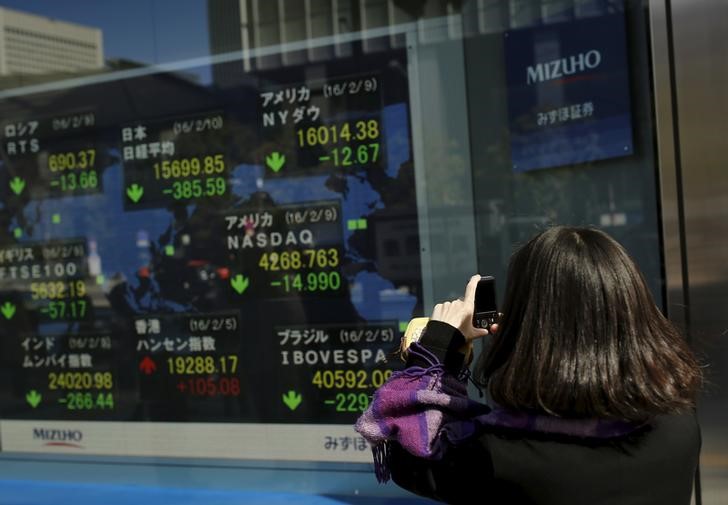 © Reuters. A woman takes pictures of display showing market indices outside a brokerage in Tokyo