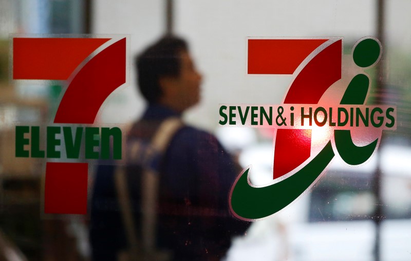 © Reuters. A shopper is seen behind a Seven & I Holdings' logo at a 7-Eleven convenience store in Tokyo