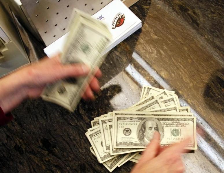 © Reuters. Four thousand U.S. dollars are counted out by a banker counting currency at a bank in Westminster