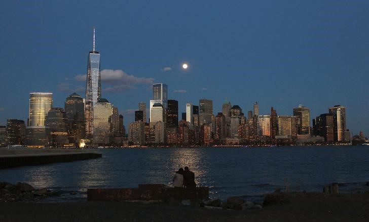 © Reuters. The moon rises behind the skyline of New York's Lower Manhattan as two people watch from a park along the Hudson River in New Jersey