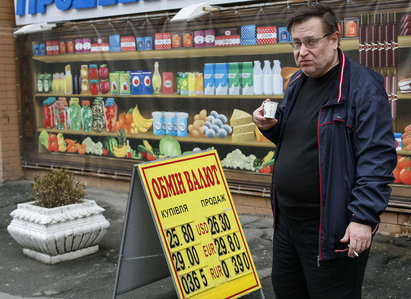 © Reuters. A man drinks coffee and smokes as he stands near a currency exchange office in Kiev