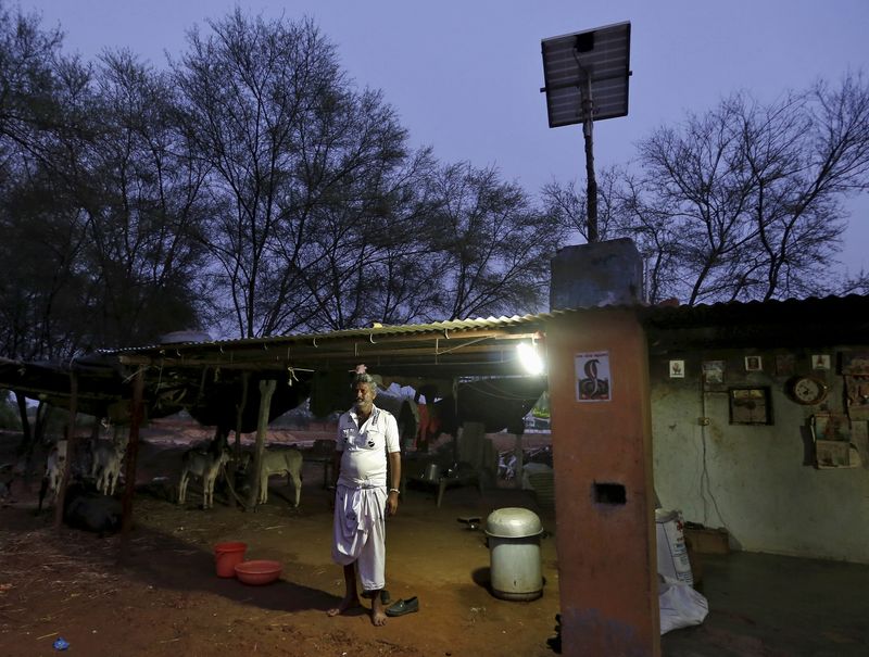 © Reuters. File photo of villager Mohan Bharwad posing next to a Compact Fluorescent Lamp powered by solar energy, outside his house on the outskirts of Gandhinagar