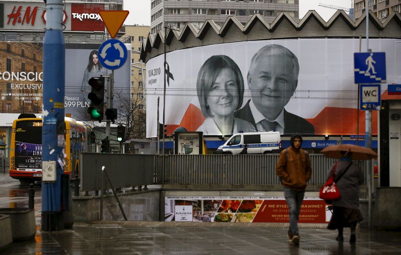 © Reuters. People walk in front of a giant picture of late Polish president Lech Kaczynski and his wife Maria, who died six years ago when a Polish government plane crashed in Smolensk, Russia, hanging on a building in the centre of Warsaw, Poland