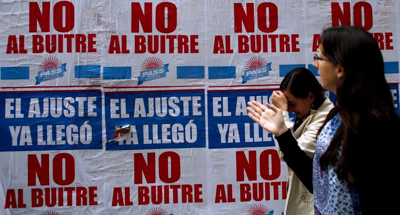 © Reuters. Women walk by posters against payment of Argentina's defaulted debt in Buenos Aires' financial district