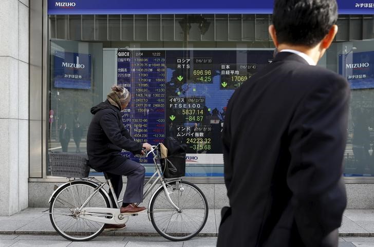 © Reuters. A man riding on a bicycle looks at an electronic board showing the stock market indices of various countries outside a brokerage in Tokyo