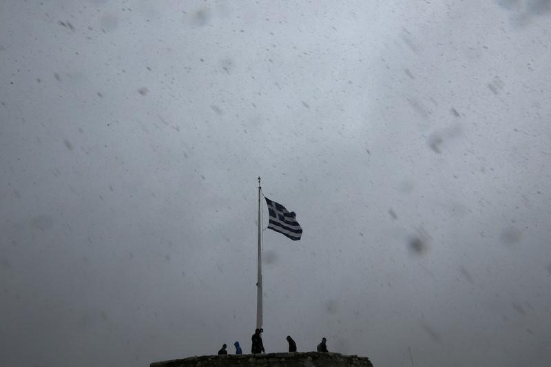© Reuters. A Greek national flag flutters atop the Athens Acropolis hill as tourists take photos during a snowstorm