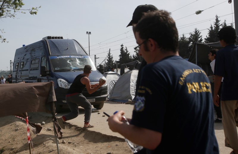 © Reuters. مهاجرون يقذفون الشرطة اليونانية بالحجارة بعدما أصابت سيارة أحدهم