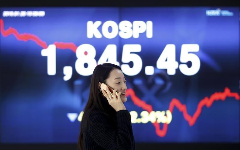 © Reuters. Seul, una donna al telefono davanti a un tabellone con l'indice di borsa sudcoreano, il Kospi