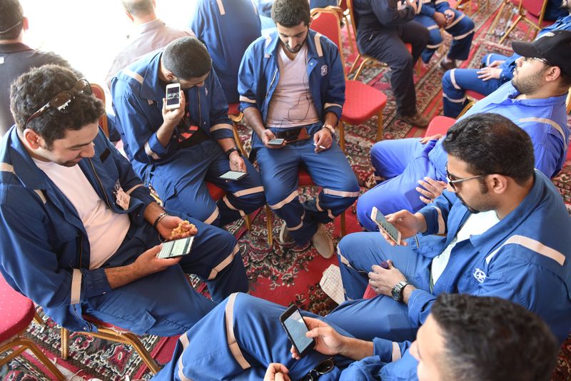 © Reuters. Kuwait Oil and Petrochemical Industries Union workers sit with their cellphones on the first day of an official strike over public sector pay reforms, in Ahmadi