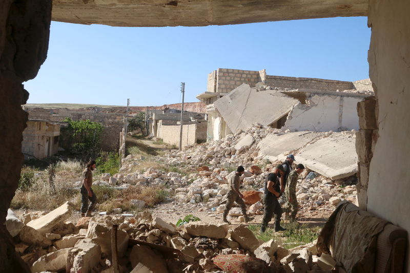 © Reuters. Harakat Nour al-Din al-Zenki fighters walk near damaged buildings in Handarat area