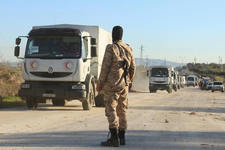 © Reuters. A rebel fighter secures a road as a Syrian Arab Red Crescent aid convoy heads towards the villages of al-Foua and Kefraya in Idlib province