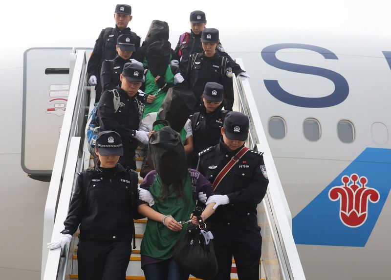 © Reuters. Police escort a group of people wanted for suspected fraud in China, after they were deported from Kenya, as they get off a plane after arriving at Beijing Capital International Airport in Beijing