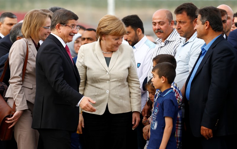 © Reuters. El primer ministro turco, Ahmet Davutoglu, y la canciller alemana, Angela Merkel, hablan con niños luego de llegar al campamento de refugiados de Nizip cerca de Gaziantep