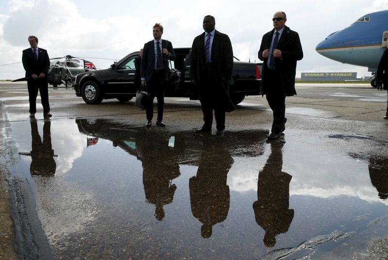 © Reuters. Security personnel are reflected in a puddle while standing before the presidential limo and Air Force One as U.S. President Barack Obama departs Stansted Airport in Stansted