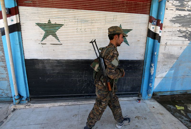 © Reuters. A Kurdish fighter from the People's Protection Units (YPG) walks past a shop with Syrian national flags painted on its shutter in the southeast of Qamishli city