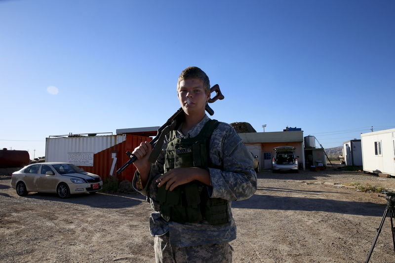 © Reuters. U.S. volunteer John Cole, 23, smokes a cigarette as he holds his assault rifle at a checkpoint in Makhmour