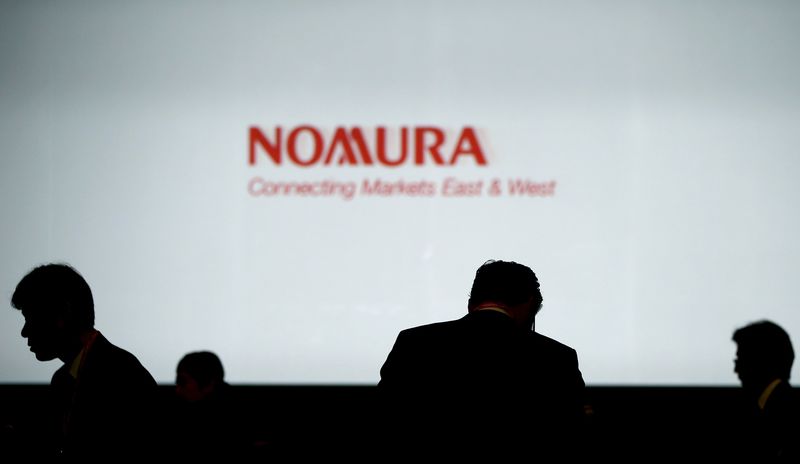 © Reuters. Investors stand in front of a screen showing the logo of Nomura Holdings in Tokyo