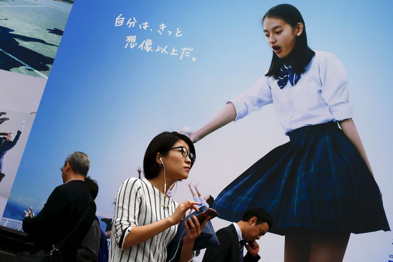 © Reuters. A woman uses her phone as she stands in front of an advertising billboard in Tokyo