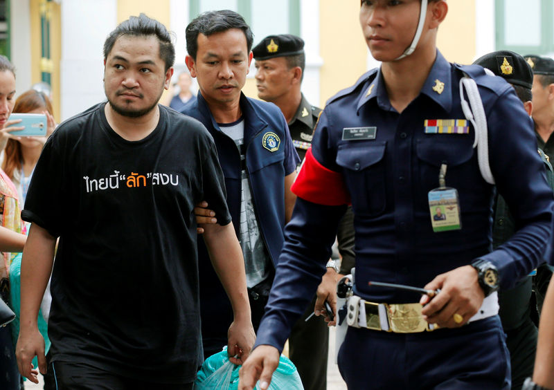 © Reuters. One of eight people charged with sedition and computer crimes  is escorted as he arrives at the military court in Bangkok