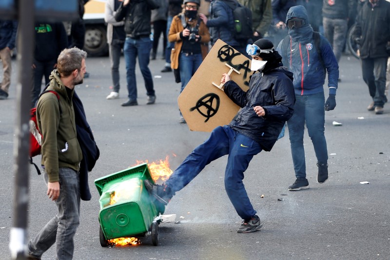 © Reuters. A masked youth kicks into a burning garbage bin during clashes in a demonstration against the French labour law proposal in Paris