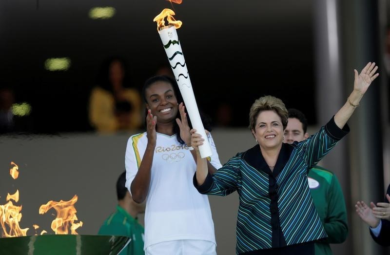 © Reuters. Brazil's President Rousseff waves after lighting a cauldron with the Olympic Flame next to Fabiana Claudino, captain of the Brazilian volleyball team, during the Olympic Flame torch relay in Brasilia