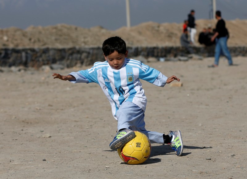 © Reuters. Five year-old Ahmadi, an Afghan Messi fan, wears a shirt signed by Barcelona star Messi, as he plays football at the open area in Kabul