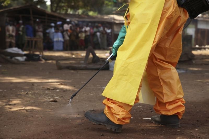 © Reuters. A member of the French Red Cross disinfects the area around a motionless person suspected of carrying the Ebola virus as a crowd gathers in Forecariah