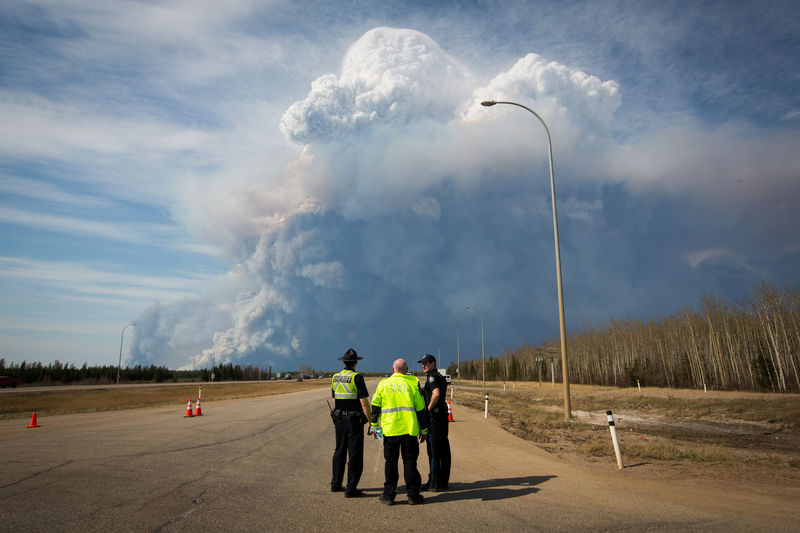 © Reuters. Officers look on as smoke from Fort McMurray's raging wildfires billow into the air after their city was evacuated