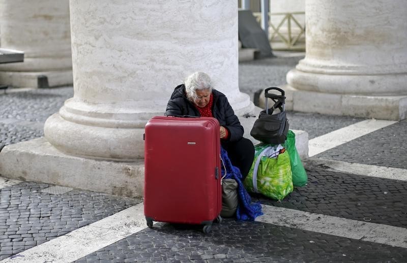 © Reuters. A homeless woman sits with her belongings as she waits for a friend coming out from the Vatican following a visit, under the Bernini's colonnade at the Vatican