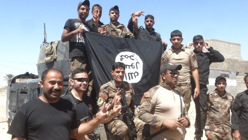 © Reuters. Iraqi security forces stand with an Islamic State flag which they pulled down in the town of Hit in Anbar province