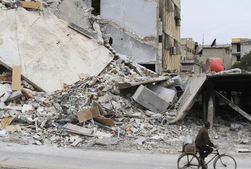 © Reuters. A man rides a bicycle past a damaged building in Daraya, near Damascus