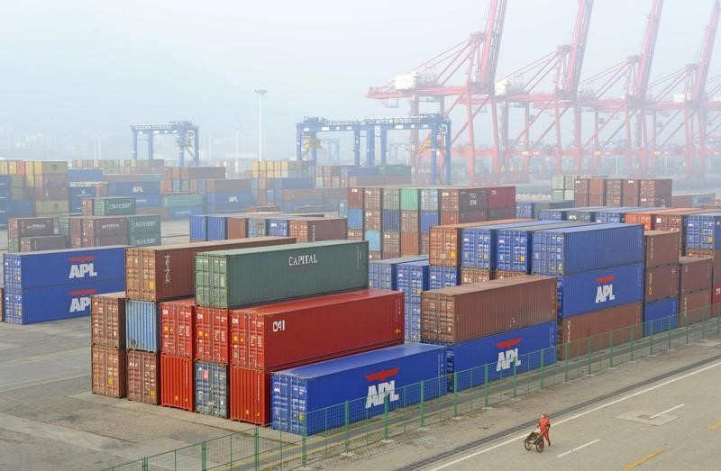 © Reuters. A worker pushes a cart next to piles of shipping containers at a port on a hazy day in Lianyungang