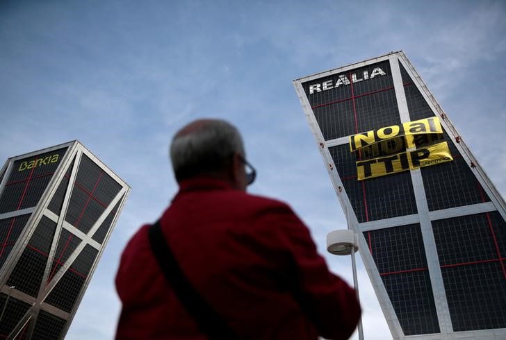 © Reuters. A man looks at Greenpeace activists displaying a banner against TTIP free trade agreement while suspended on one of the Kio towers in Madrid