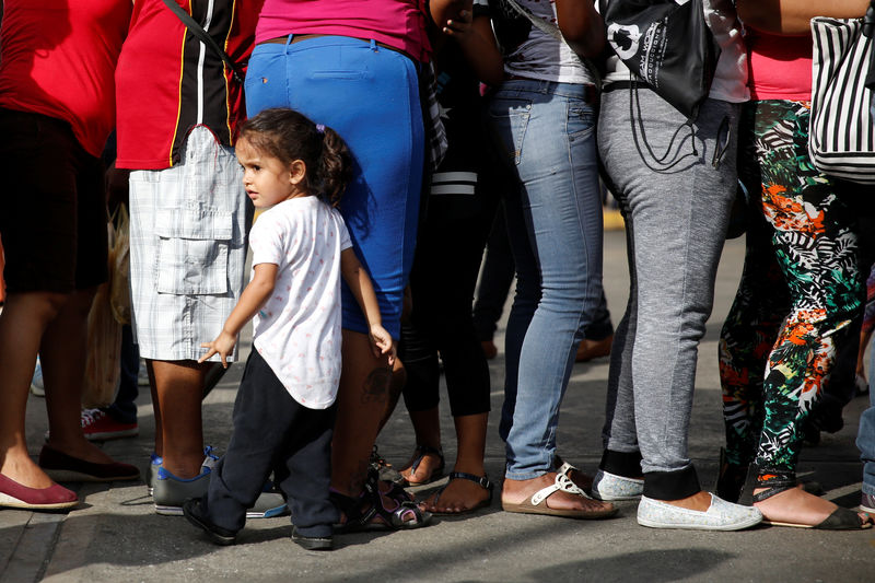 © Reuters. A girl stands next to her mother while they queue next to others to try to buy toilet paper and diapers outside a pharmacy in Caracas