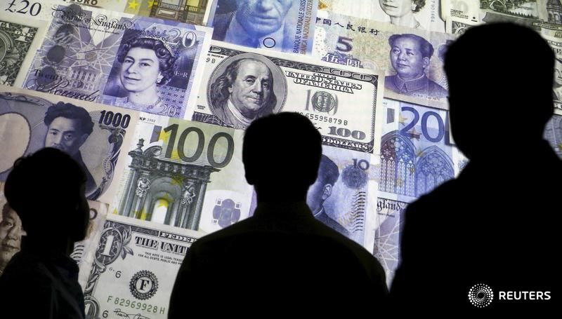 © Reuters. Силуэты людей на фоне изображений валют различных стран 